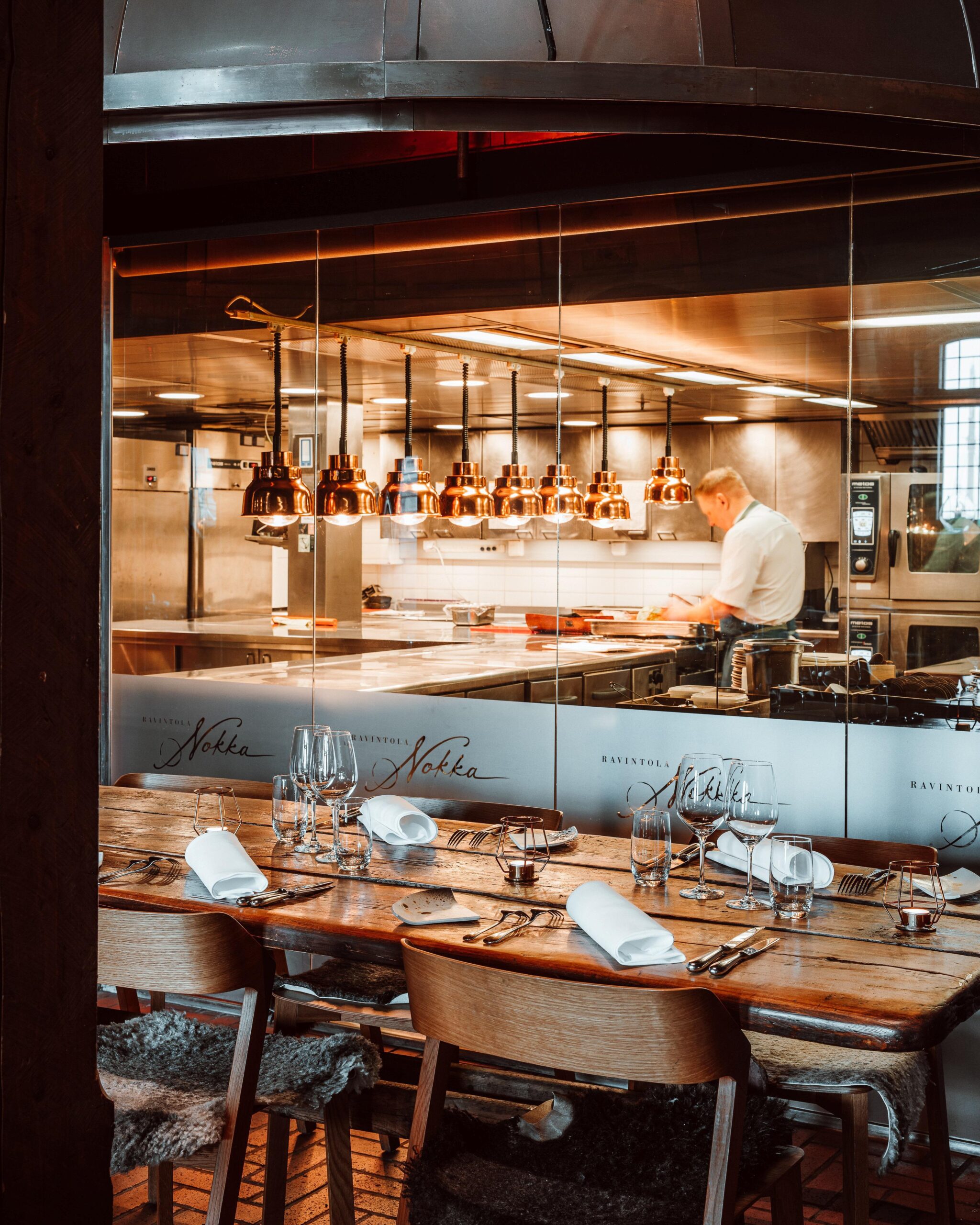 Restaurant Nokka's interior. Tables can be seen in the picture, and in the kitchen in the background there is a cook.