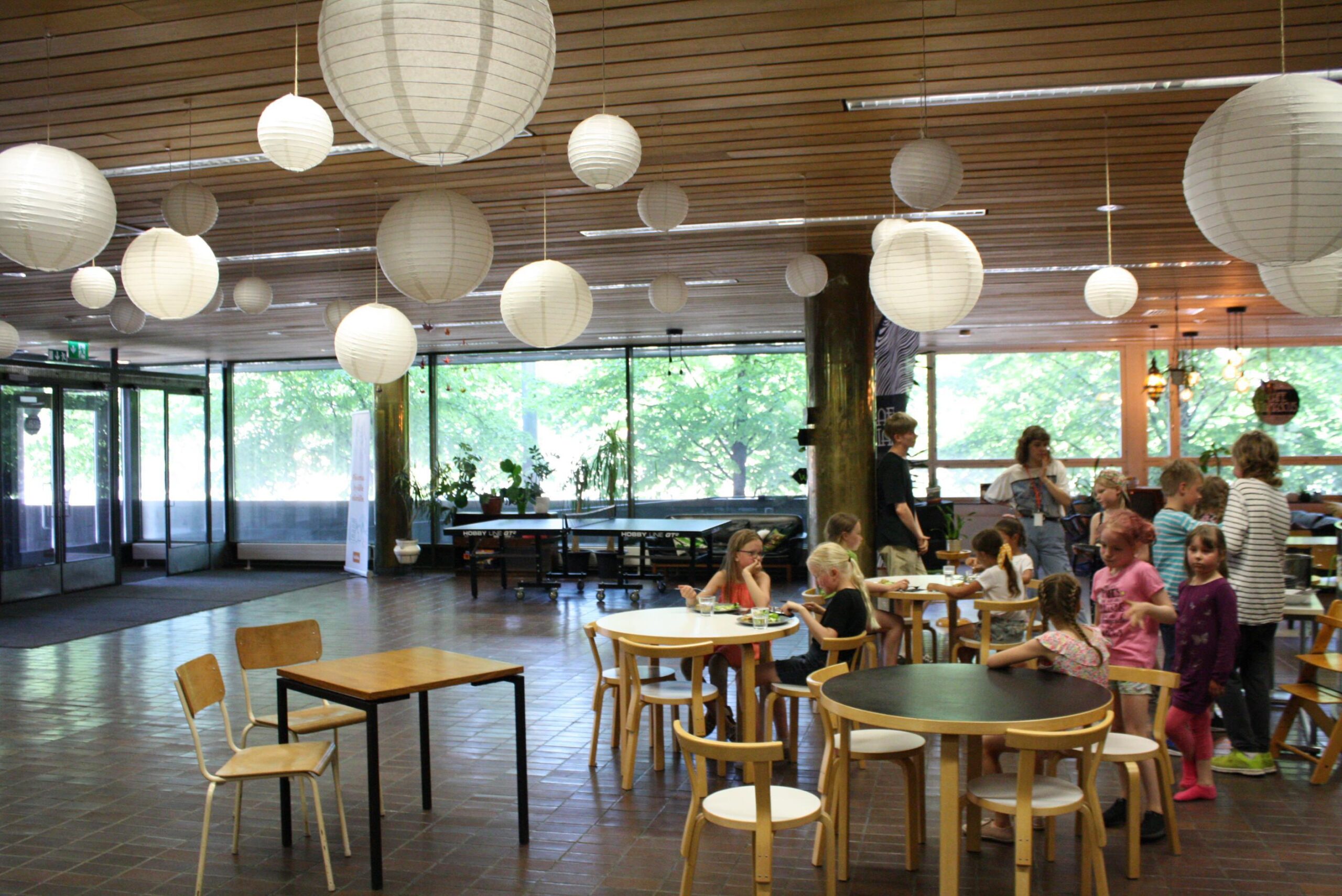 In the picture, the lobby of the Settlement House, with tables and children sitting by them.