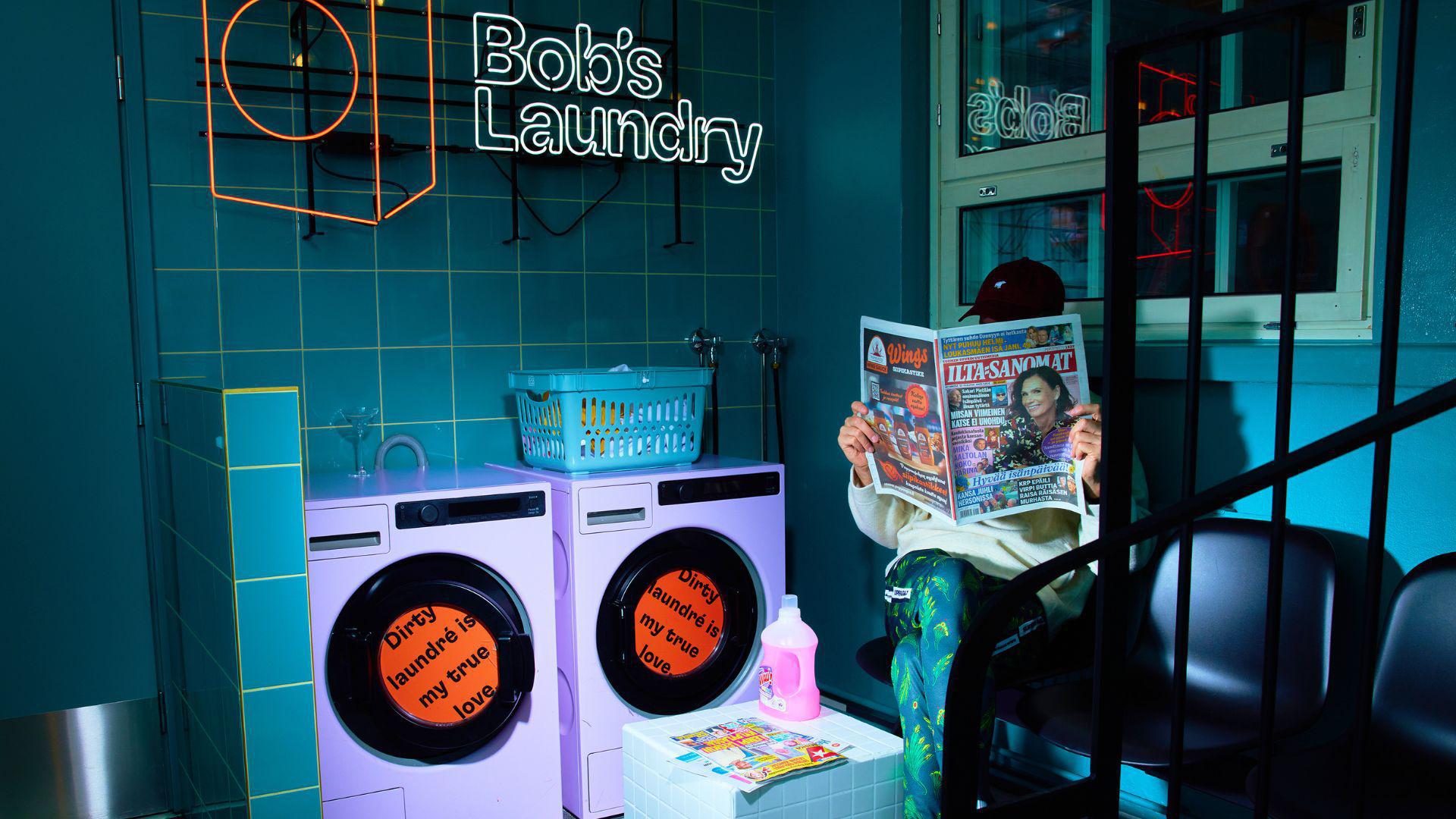 Bob's Laundryn sisätilat. Henkilö istuu sanomalehti kädessä kahden pesukoneen vieressä.