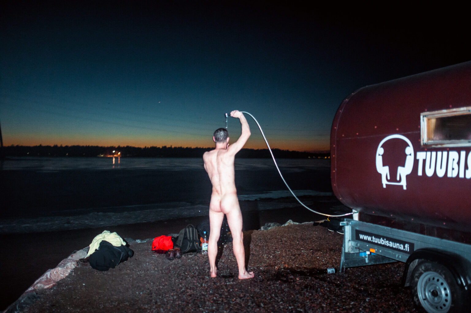 Man taking a shower by homemade sauna truck in Helsinki