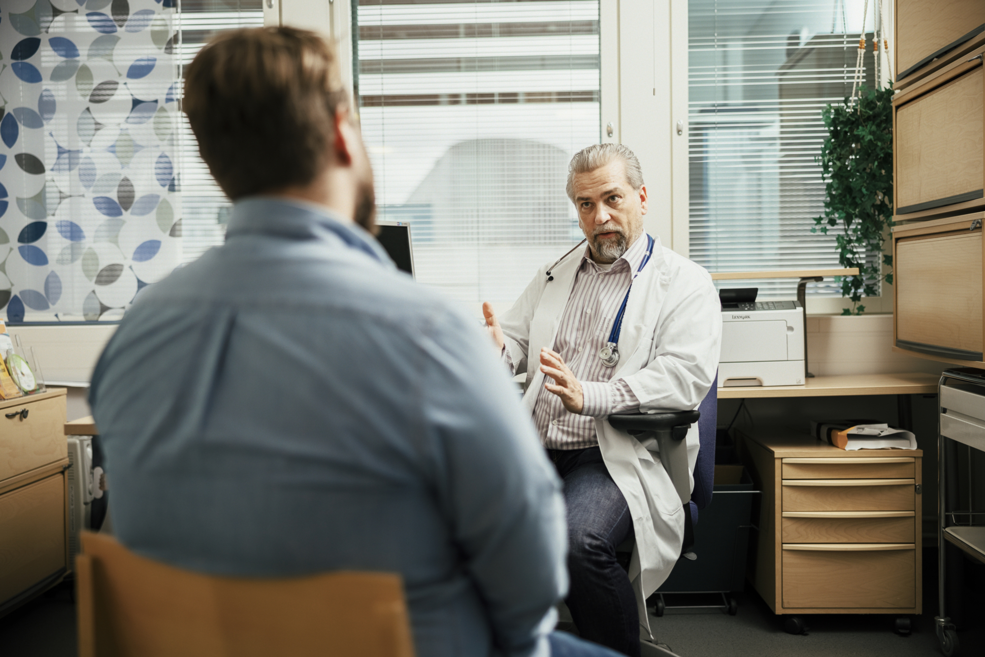 a doctor in a white coat talking to a man in a chair a typical scene in healthcare in Finland