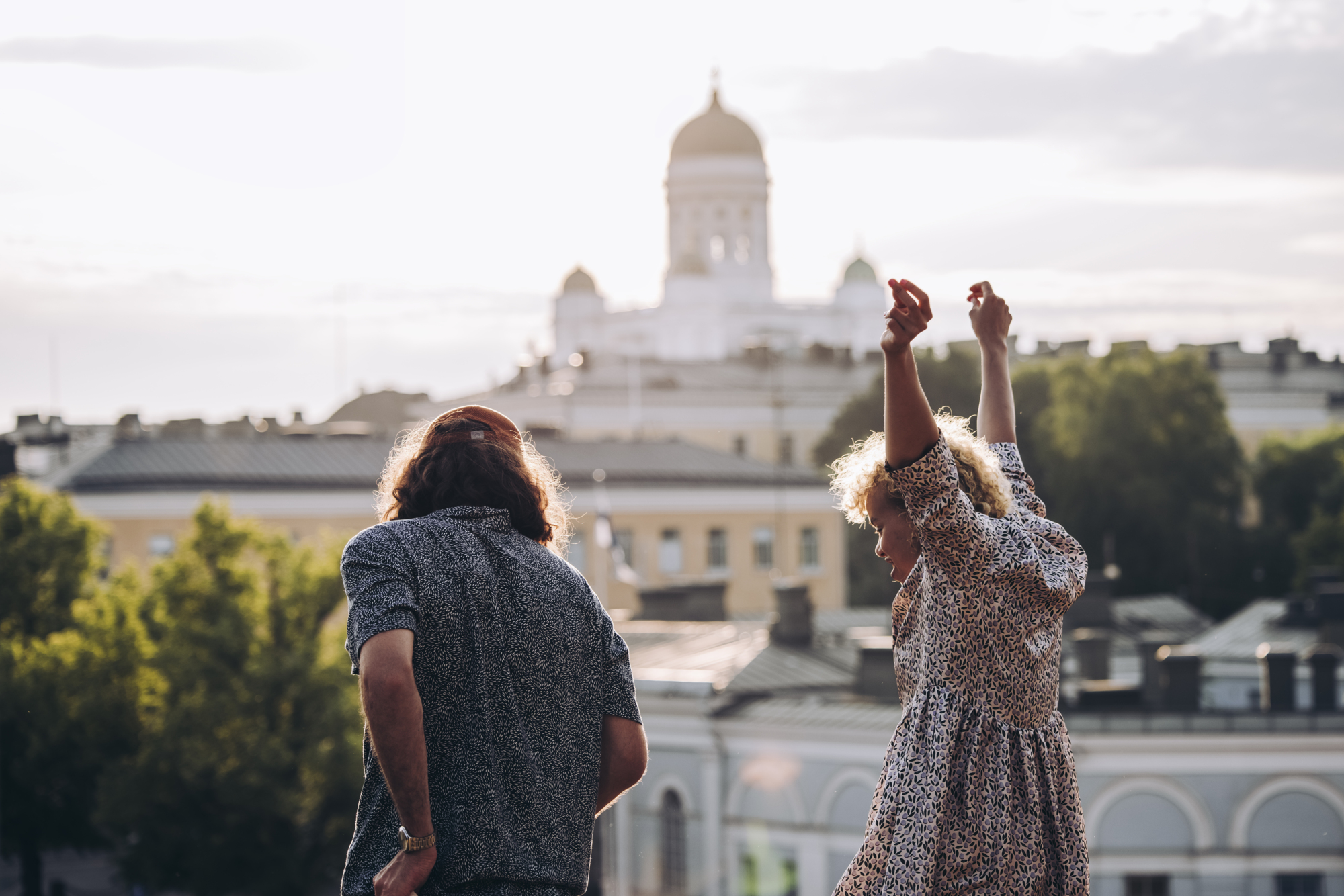 a man and woman standing on a hill with their arms raised