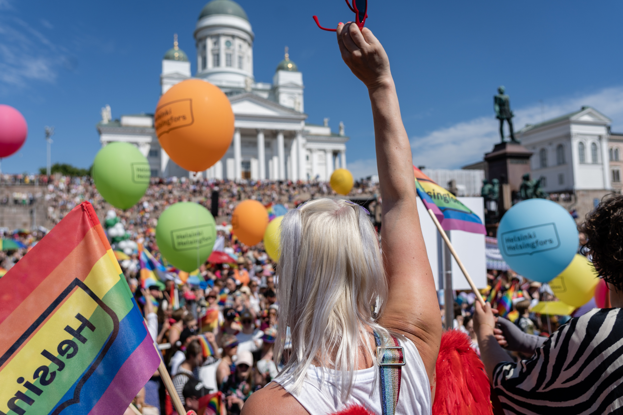 a woman holding up a red sunglasses in front of a crowd of people at Pride Helsinki