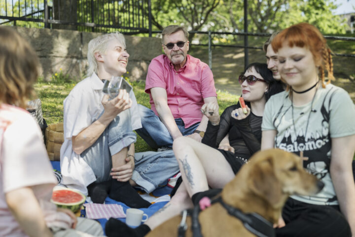 a group of people old and young sitting on a blanket in the summer