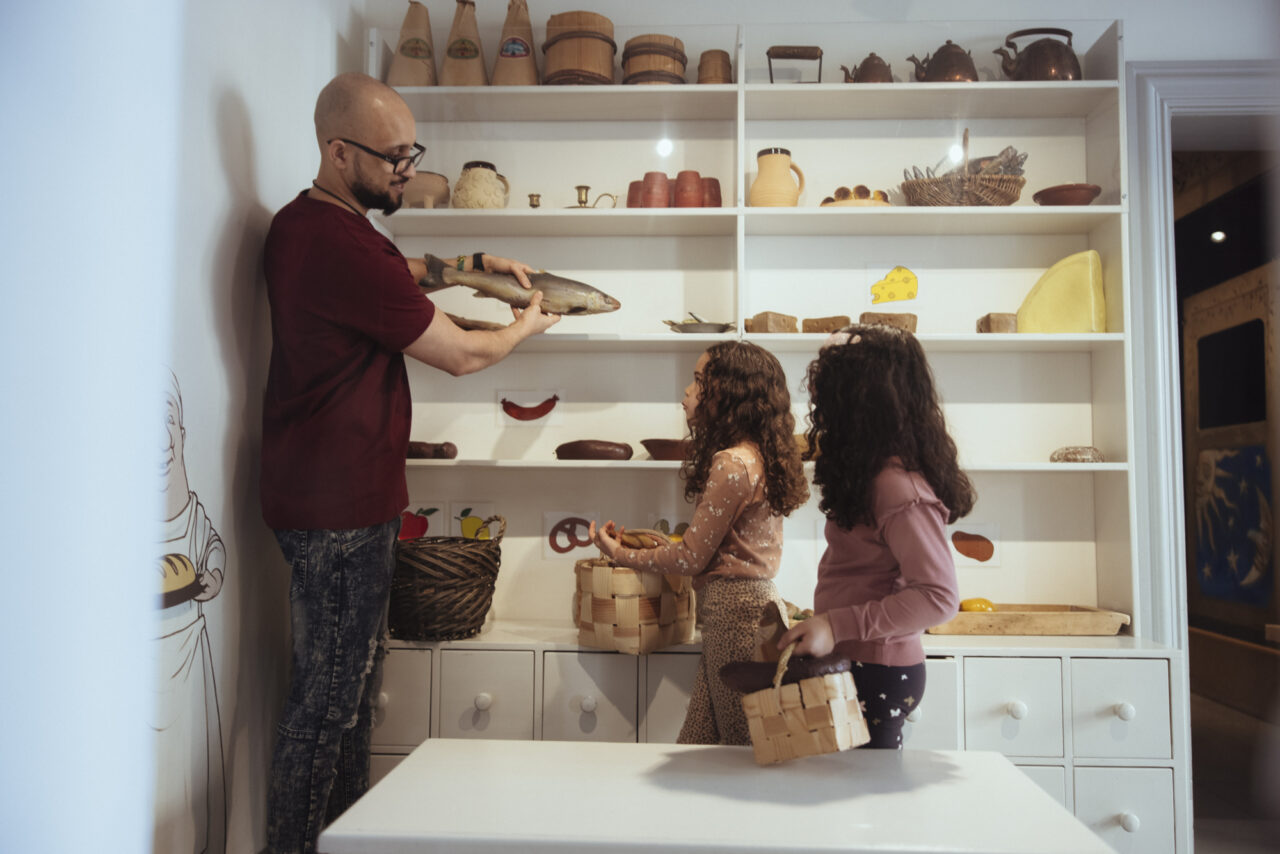 a man holding a fish in a kitchen with two young girls