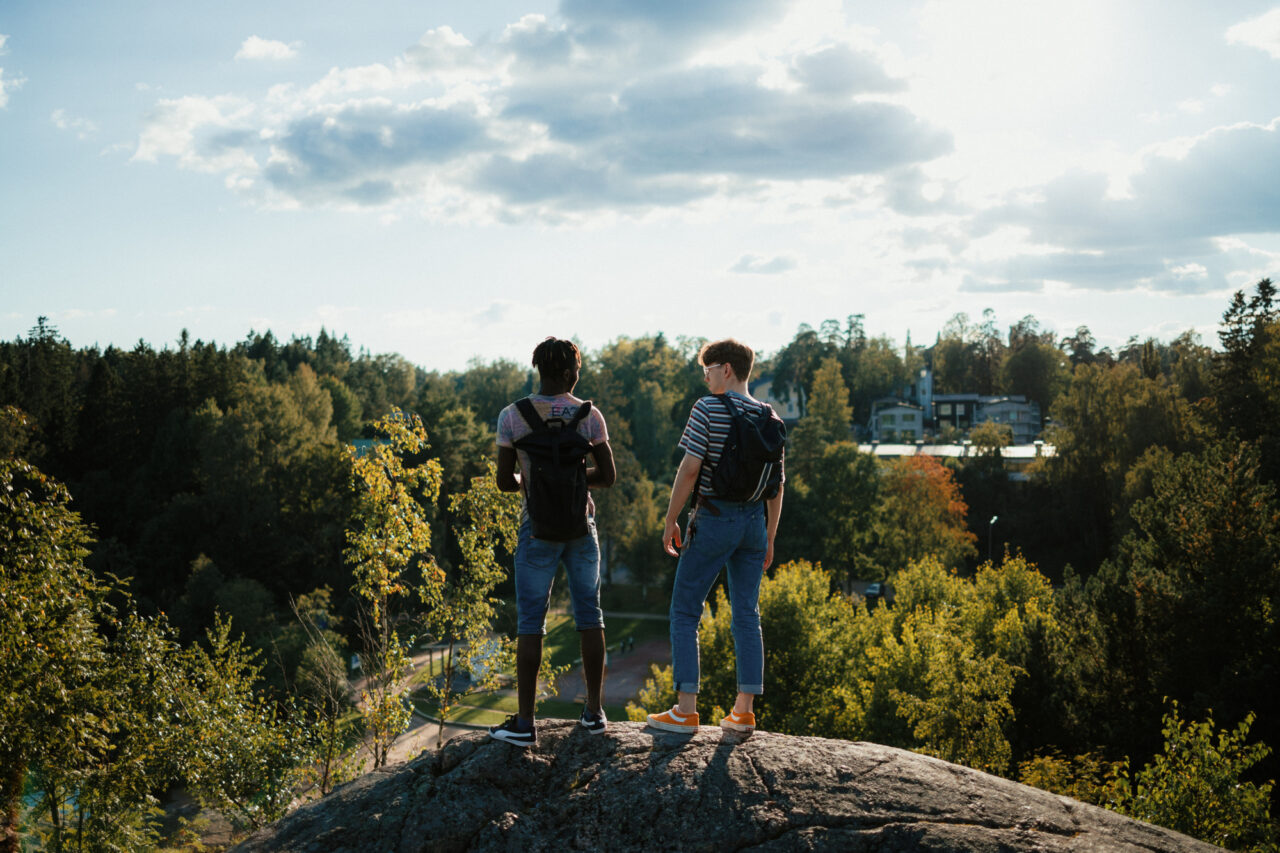 two men standing on a rock looking at trees